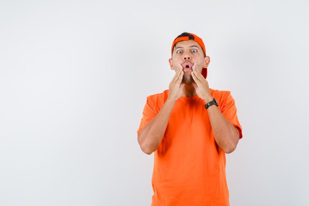 Jeune homme tenant la main près de la bouche en t-shirt orange et casquette et à la peur