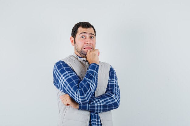 Jeune homme tenant la main sur sa mâchoire en chemise, veste sans manches et regardant anxieux, vue de face.