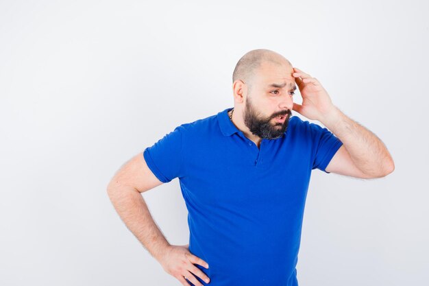 Jeune homme tenant la main sur sa tête tout en parlant en chemise bleue et l'air troublé, vue de face.