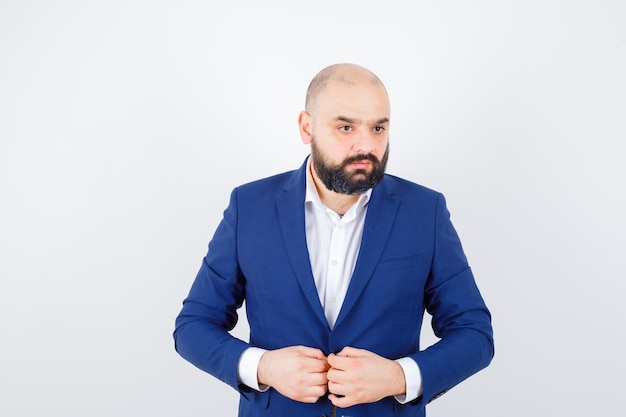 Jeune homme tenant la main sur sa veste en chemise blanche, veste et à l'air pensif. vue de face.