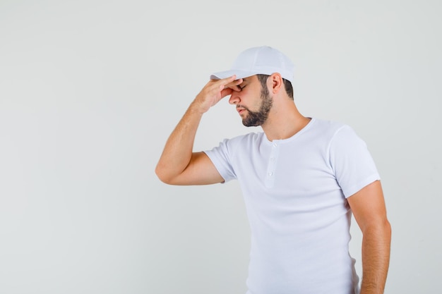 Jeune homme tenant la main sur son front en t-shirt blanc et l'air fatigué. .