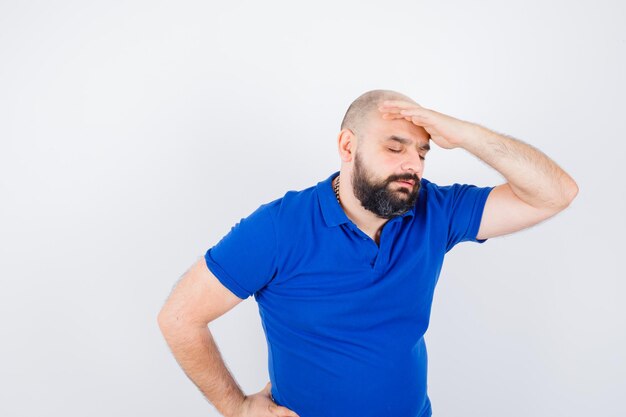 Jeune homme tenant la main sur la tête en chemise bleue et à la recherche de stress. vue de face.