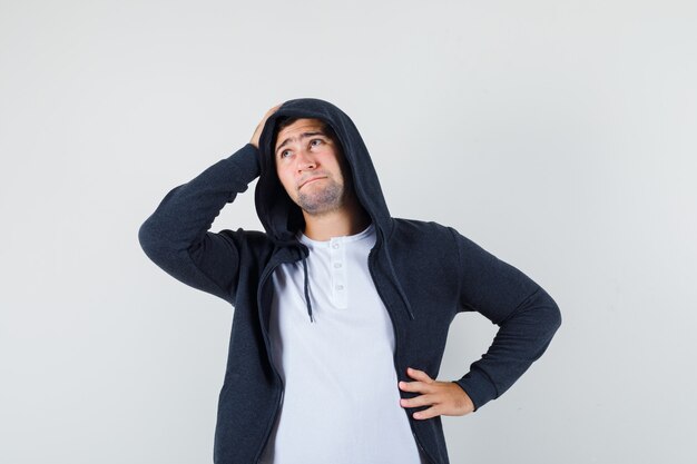 Jeune homme tenant la main sur la tête en t-shirt, veste et regardant impuissant, vue de face.