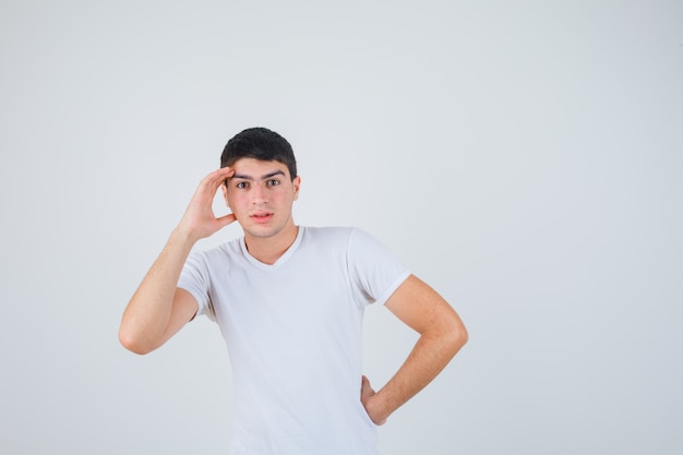 Jeune Homme Tenant La Main Sur La Tête En T-shirt Et à La Vue De Face, Focalisée.