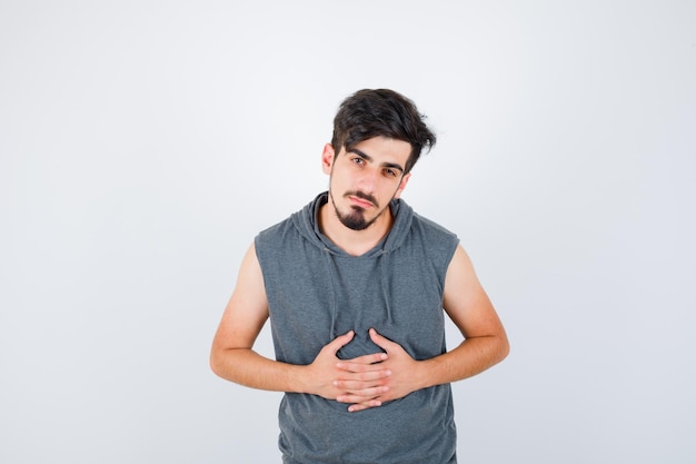 Jeune homme tenant la main sur le ventre en t-shirt gris et à la grave