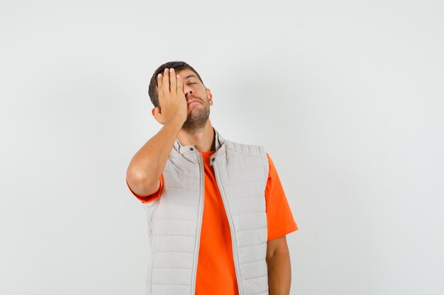 Jeune homme tenant la main sur le visage en t-shirt, veste et regardant pensif. vue de face.