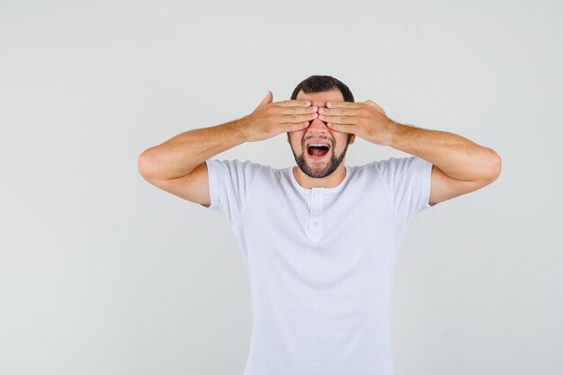 Jeune homme tenant la main sur les yeux en t-shirt et l'air timide, vue de face.