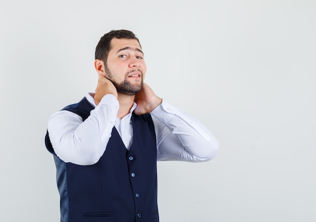 Jeune homme tenant les mains sur le cou en chemise, vue de face de gilet.