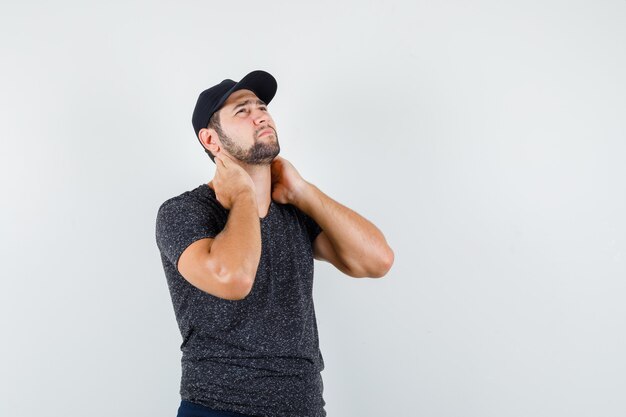 Jeune homme tenant les mains sur le cou en t-shirt et casquette, jeans et à la triste