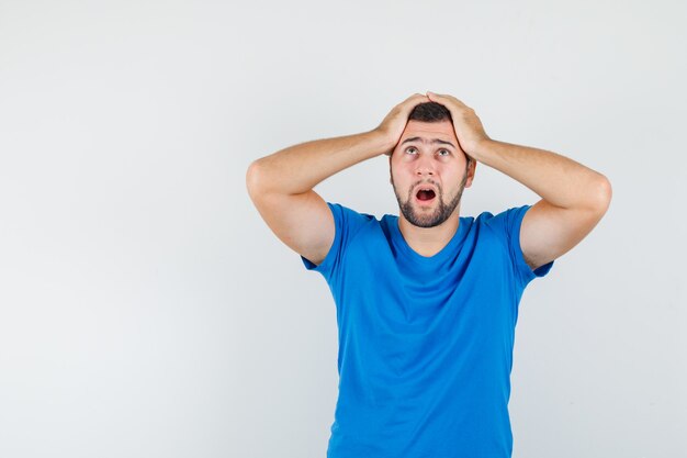 Jeune homme tenant les mains sur la tête en t-shirt bleu et à la recherche d'impuissance