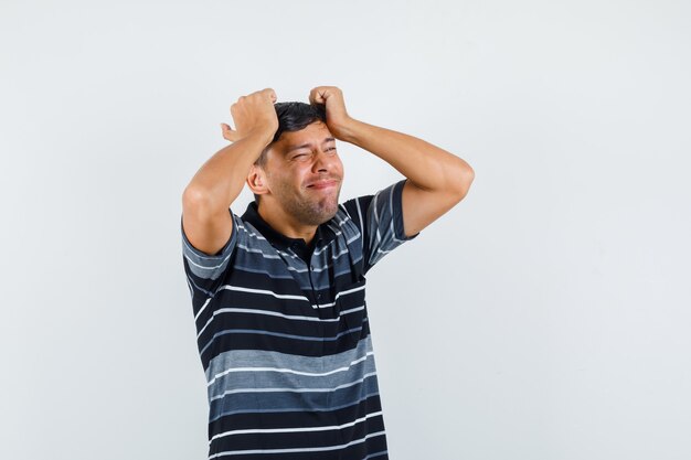 Jeune homme tenant les mains sur la tête en t-shirt et regardant triste, vue de face.