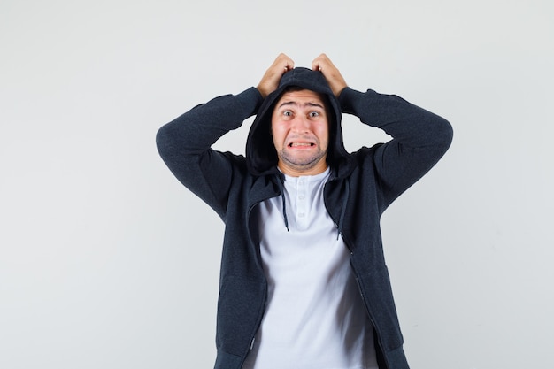 Jeune homme tenant les mains sur la tête en t-shirt, veste et regardant anxieux, vue de face.