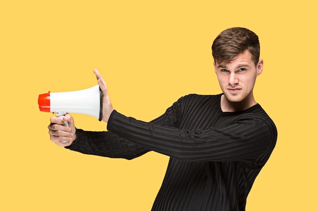 Jeune homme tenant un mégaphone sur fond de studio jaune