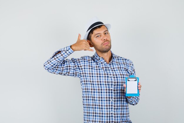 Jeune homme tenant un mini presse-papiers, montrant le geste du téléphone en chemise à carreaux