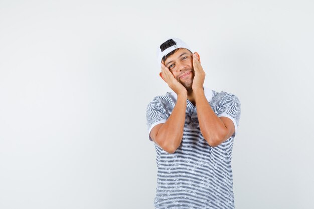 Jeune homme tenant des paumes sur les joues en t-shirt et casquette et à mignon