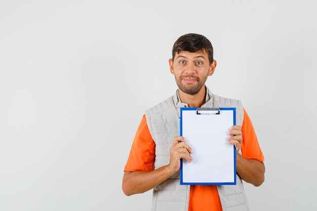 Jeune homme tenant le presse-papiers et le crayon en t-shirt, veste et à la joyeuse.