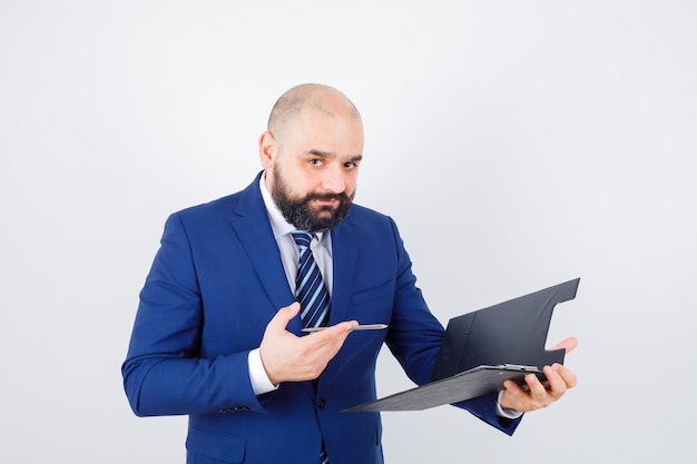 Jeune homme tenant un presse-papiers, un stylo en chemise blanche, une veste et l'air confiant, vue de face.