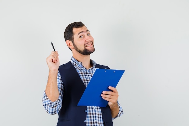 Jeune homme tenant le presse-papiers et un stylo en chemise, gilet et à la joyeuse