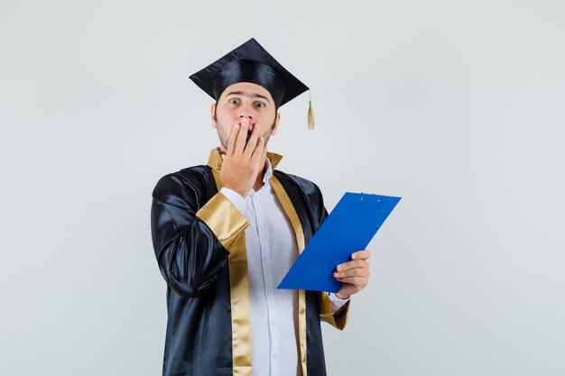 Jeune homme tenant le presse-papiers en uniforme d'études supérieures et à la vue de face, oublieux.