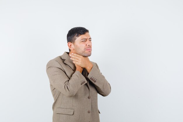 Jeune homme tenant sa gorge en veste marron grisâtre et à la vue de face, malade.