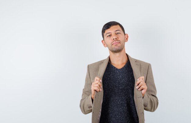 Jeune homme tenant sa veste en veste marron grisâtre, chemise noire et à la confiance. vue de face.