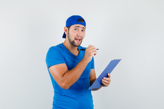 Jeune homme tenant un stylo et un presse-papiers en t-shirt bleu et une casquette