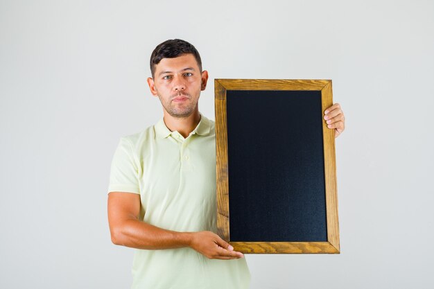 Jeune homme tenant un tableau noir et regardant la caméra en t-shirt