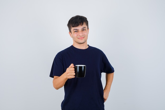 Jeune homme tenant une tasse de boisson en t-shirt noir et regardant fier, vue de face.