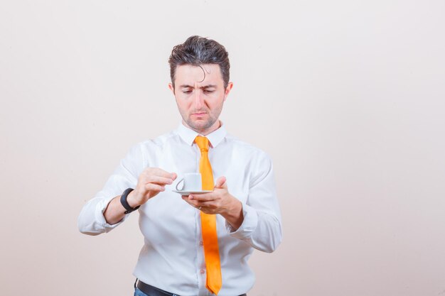 Jeune homme tenant une tasse de café renversée en chemise blanche