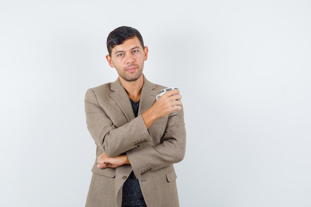 Jeune homme tenant une tasse en veste marron grisâtre et à la recherche de calme. vue de face.