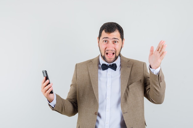 Jeune homme tenant un téléphone mobile en costume et à la recherche d'anxiété. vue de face.