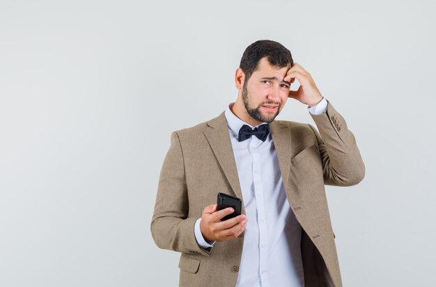 Jeune homme tenant un téléphone mobile en costume et à la recherche d'oubli. vue de face.