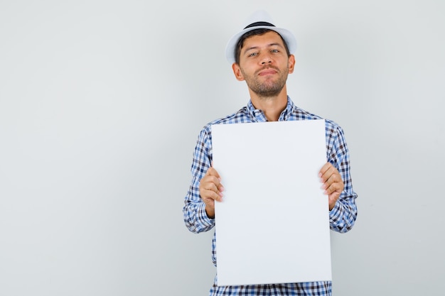 Photo gratuite jeune homme tenant une toile vide en chemise à carreaux