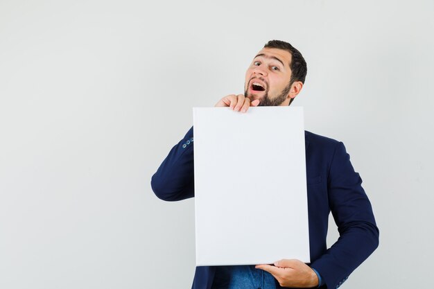 Jeune homme tenant une toile vierge en chemise, veste et à la gaieté. vue de face.