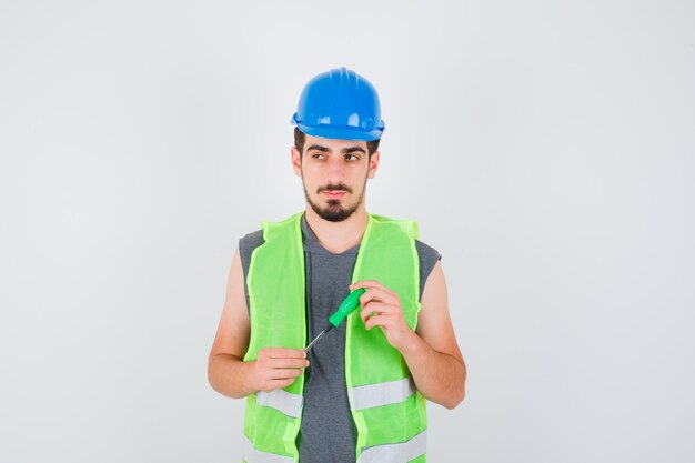 Jeune homme tenant un tournevis, à l'écart en uniforme de construction et à l'air pensif