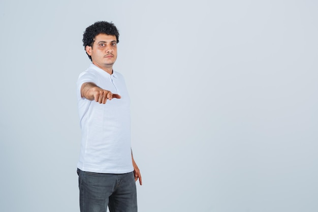 Jeune homme tendant la main vers la caméra en t-shirt blanc et jeans et regardant sérieux, vue de face.