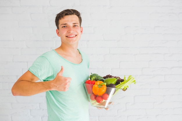 Jeune homme, tenue, légumes frais, dans, verre, bol, projection, pouce vers le haut, signe