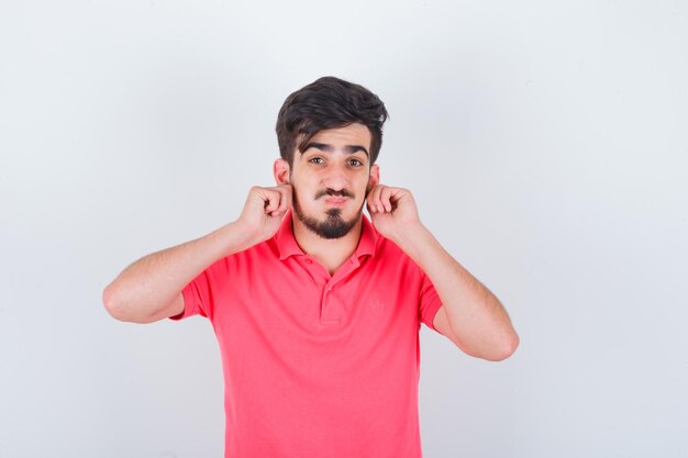 Jeune homme tirant les oreilles en t-shirt rose et l'air mignon. vue de face.