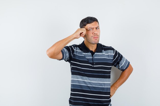 Jeune homme tirant la peau sur ses tempes en t-shirt et ayant l'air sérieux. vue de face.