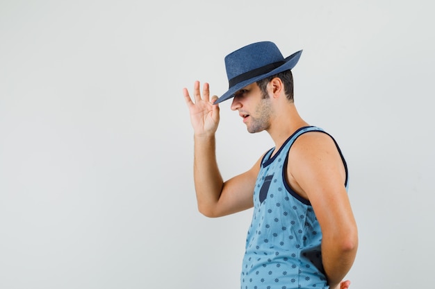 Jeune homme tirant vers le bas chapeau sur les yeux en maillot bleu et à l'élégant.