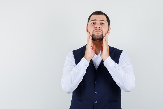 Jeune homme touchant la mâchoire en chemise et gilet et à la confiance