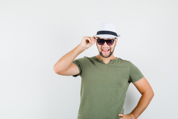 Jeune homme touchant ses lunettes en t-shirt vert et chapeau et à la bonne humeur