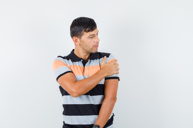 Jeune homme touchant son bras tout en regardant de côté en t-shirt et à la pensif