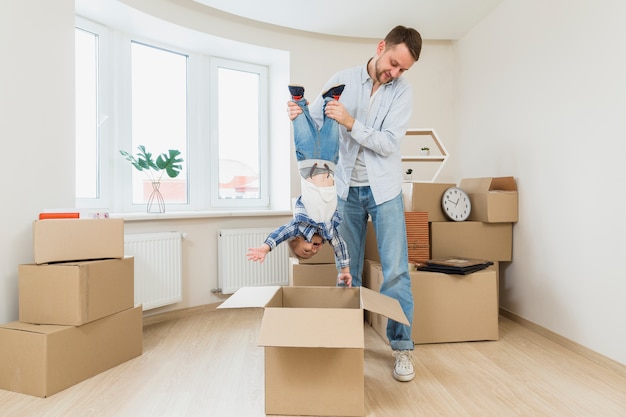 Jeune homme transportant son fils d&#39;enfant en bas âge à l&#39;envers sous la boîte en carton à la nouvelle maison