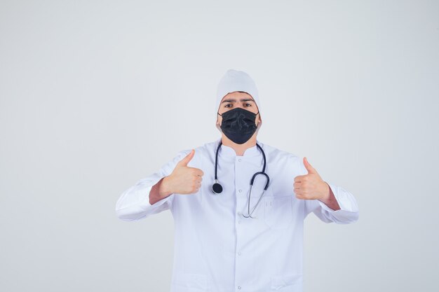 Jeune homme en uniforme blanc, masque montrant les pouces vers le haut et à la confiance