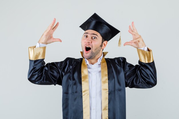 Jeune homme en uniforme diplômé levant les mains et à la vue étonnée, de face.