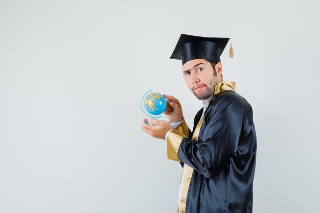 Jeune homme en uniforme d'études supérieures choisissant la destination sur le globe de l'école et à la recherche d'indécis.