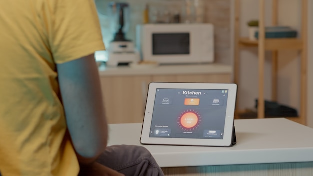 Jeune homme utilisant une application de maison intelligente avec commande vocale pour allumer la lumière avec une tablette numérique