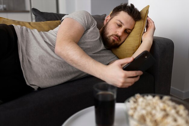 Jeune homme utilisant son smartphone à la maison sur le canapé