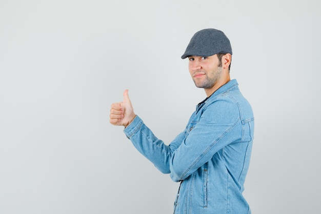 Jeune homme en veste, casquette montrant le pouce vers le haut et à la recherche de confiance.